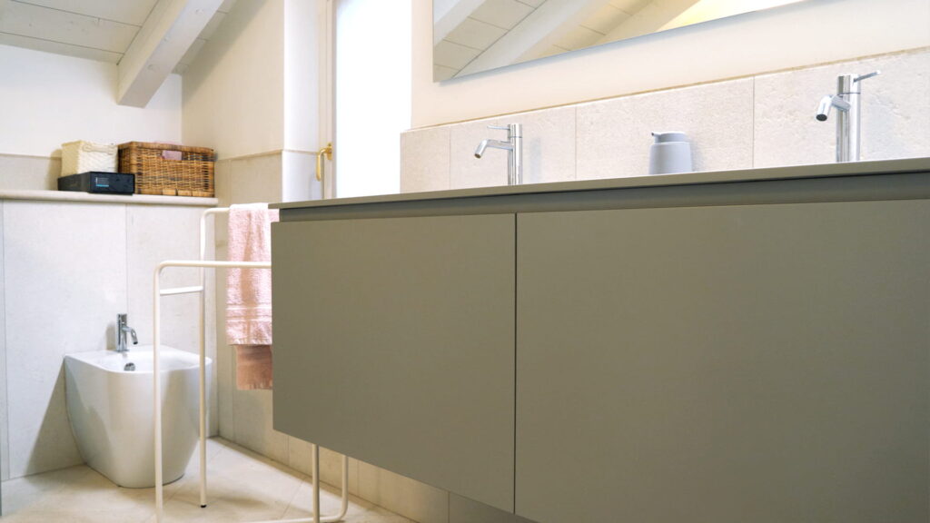 Mobile bagno sospeso grigio tortora con doppio piano in gres e rubinetteria cromata, bidet e porta asciugamani in metallo bianco, rivestimento in pietra chiara